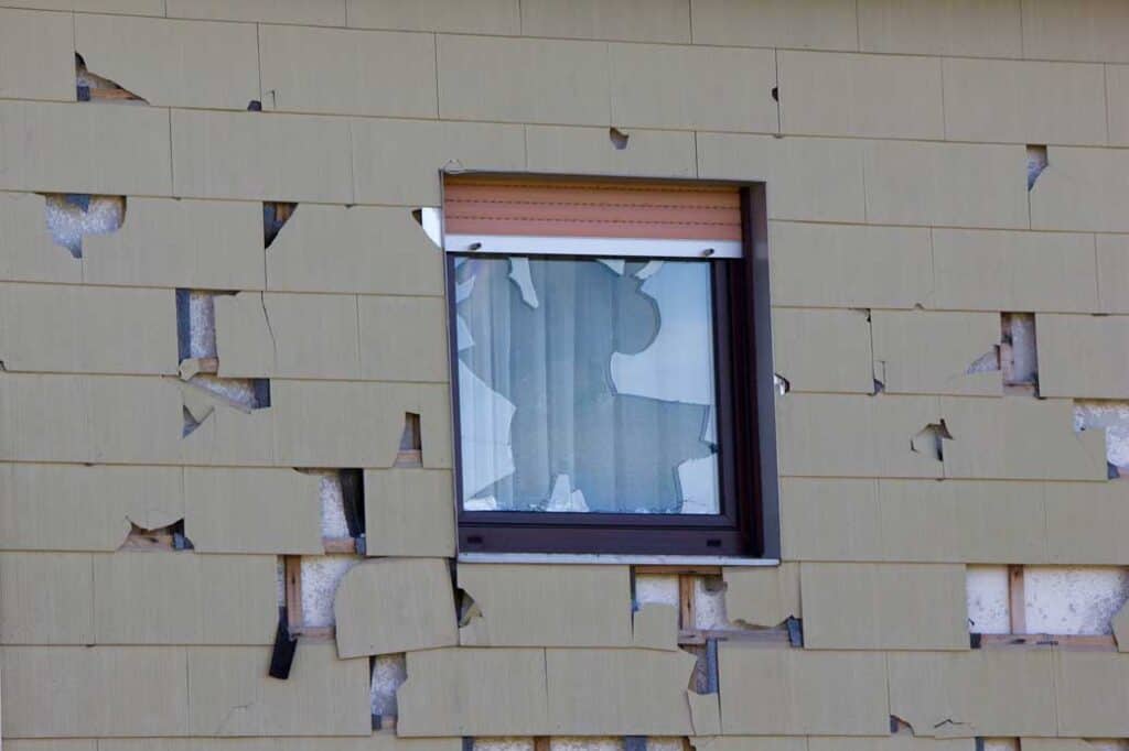A window surrounded by damaged vinyl siding.