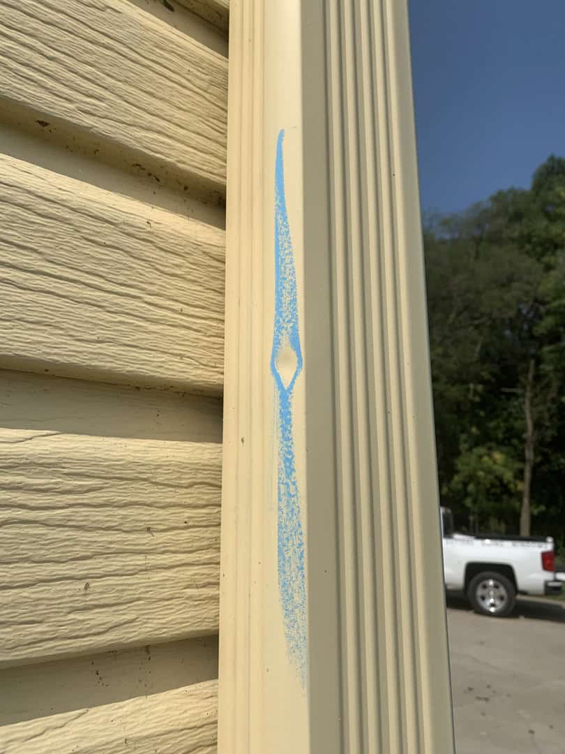Hail damage highlighted by roofer's chalk on an Omaha home's downspout of the gutter system