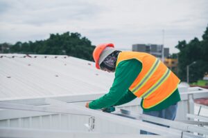 Omaha roofer in safety vest cleaning a PVC commercial roof