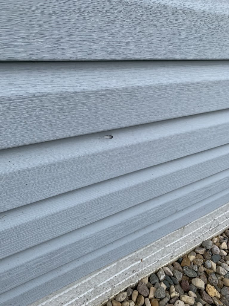 Hole in vinyl siding on Omaha home caused by recent hail storm.